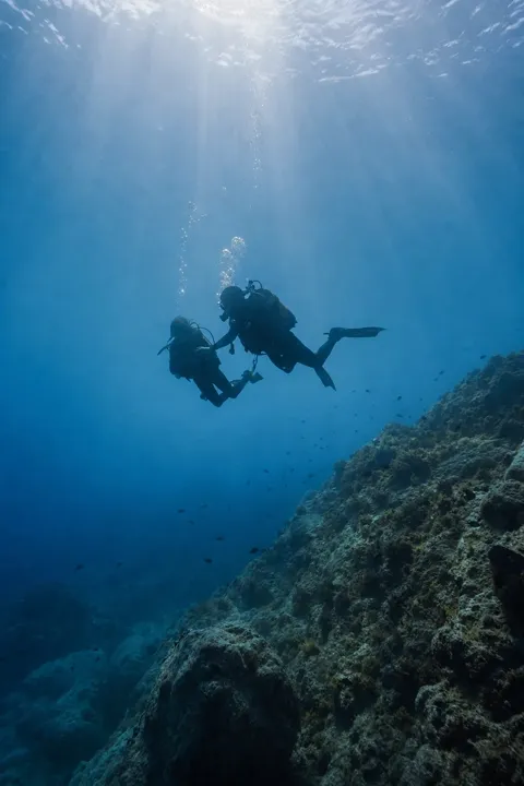 Silhouettes d'un plongeur et de son moniteur au-dessus d'un tombant méditerranéen